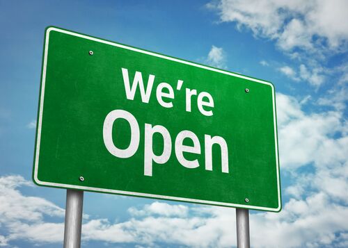 Large green traffic sign with white text saying we are open