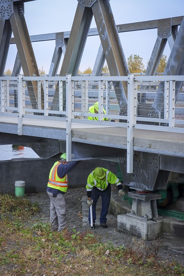 Photograph of Construction workers on a bridge and below the bridge working